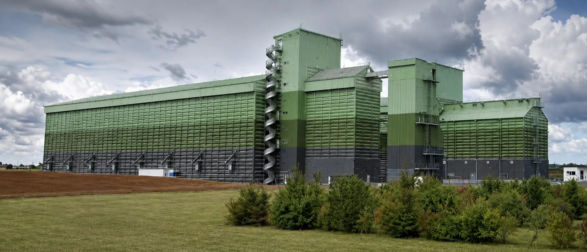 Le même bâtiment de stockage après intervention, dégradé de verts sur les claires-voies et soubassement anthracite.