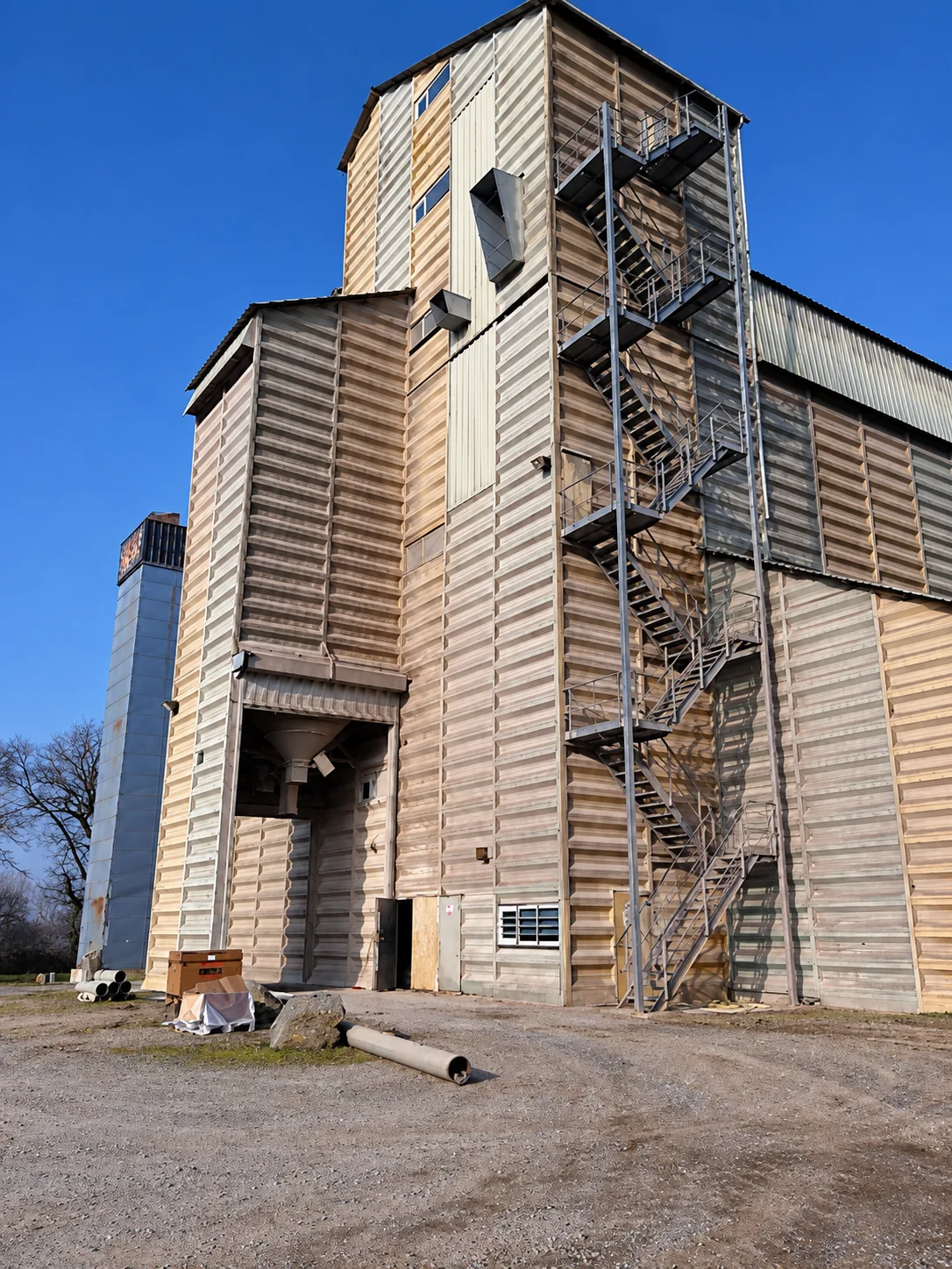 Tour de silo avant intervention, bardage oxydé et strié, escalier métallique, vue en contre-plongée.